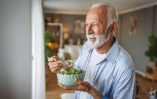 Senior man eating a salad while looking out a window. 